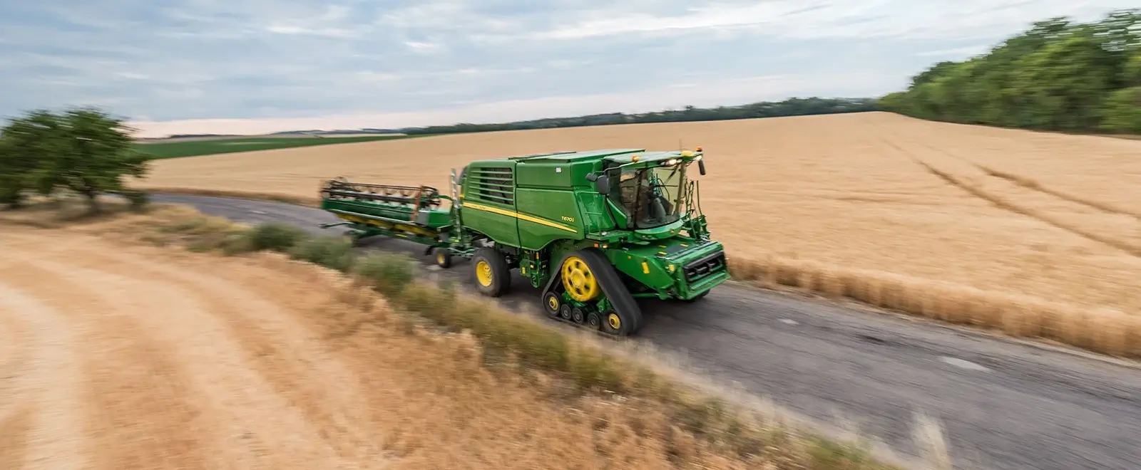 Transportwagen hinter Landmaschine auf der Straße zwischen gemähten Feldern